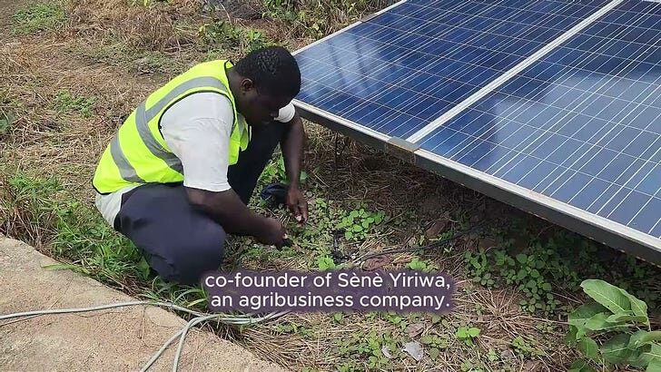 Boubou D. crouches beside a solar panel array, working on an irrigation installation for Sènè Yiriwa.