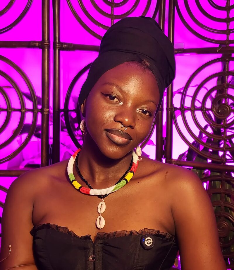 Mona S., a Kabakoo learner from Burkina Faso in the Fashion and Music Biz Track, photographed against a pink woven background.